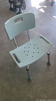 Light green plastic shower chair with backrest and adjustable legs, shown from front angle on concrete floor.