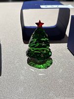 Green faceted Swarovski crystal Christmas tree with red star topper placed on surface.