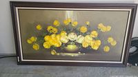 Framed oil painting of yellow and white roses in a vase on a table, muted background.