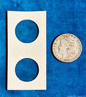 Coin placed next to two-hole cardboard slide on blue background