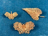 Three 800 silver filigree brooches on blue fabric background, shows one butterfly brooch smaller, one butterfly larger, and one leaf-shaped brooch.