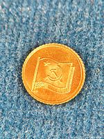 Close-up image of the gold medal front side showing the flag with hammer and sickle detail on a textured blue background.