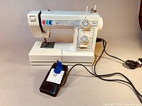 Full view of the white Janome sewing machine with foot pedal and cord included on a beige surface.