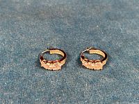 Pair of small silver hoop earrings with clear zirconia stones, displayed on blue fabric.