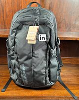 Front view of new black Patagonia Refugio backpack with integral LinkedIn patch and attached tags.
