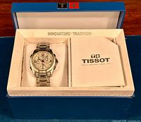 Watch with bracelet and branded papers displayed in Tissot presentation box lined with cream insert and blue outer case