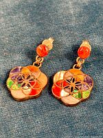 Pair of colorful handmade silver earrings laid on blue fabric, showing floral design with multi-colored inlay stones and shell