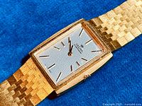 Close-up front view of watch face and part of gold-plated bracelet laid on blue background