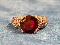 Close-up front view of the ring showing the deep red garnet stone and detailed silver-toned filigree band.