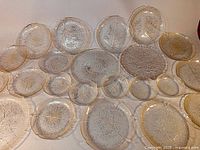 Photo shows a large assortment of clear vintage pressed glass plates and bowls with detailed Aspen leaf embossed patterns laid out flat showing variety in size and shape.