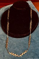 Full view of the necklace displayed on a black jewelry bust showing the complete length and sculptural half-circle segment design on a teal cloth.