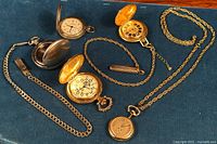 Five vintage quartz pocket watches displayed on blue fabric, showing varying chain lengths, case finishes, and watch face designs.
