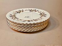 Stack of seven Royal Albert Brigadoon bone china dinner plates showing scalloped edges and floral gilded design