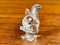 Clear Swarovski crystal squirrel figurine holding a nut, front angle view showing detailed faceting and black eyes.