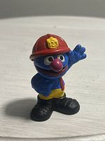 Front view of Grover firefighter figure with red helmet '123' and a waving pose