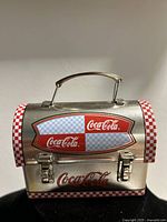 Front view of small Coca-Cola metal keepsake box with handle and latch, showing checkered pattern and logo.