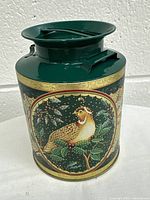 Front view of decorative green tin can showing bird painting and gold trim.
