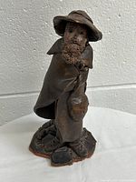 Front view of the clay figurine showing the bearded man with hat and cloak holding a lantern.