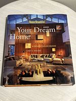 Front cover of the hardcover home design book showing modern living room interior design with couches, wood panel walls, and candles on a table.
