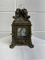Front view showing the decorative elephants, framed photo on front, and claw feet base.