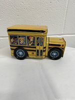 Front and side view of the yellow metal tin school bus coin bank showing illustrated windows with passengers, wheels, and bus number 22