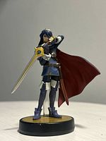 Front view of Lucina Amiibo figure with sword and red cape on black and gold base.