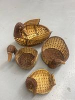 Four brown wicker baskets shaped like ducks in varying sizes displayed on the floor, showing the woven duck head detail and body basket shape.