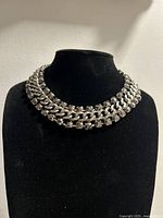 Front view of silver chain necklace on black display bust showing double rows of links and stones.