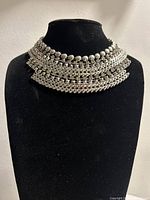 Front view of silver metal choker necklace showing fishbone style linked structure and round metal beads arranged in multiple rows for texture.