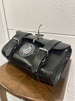 Front angle view of black leather motorcycle tool bag with Indian Motorcycle logo showing buckle closures and overall shape.