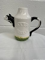 Side view showing the cow head spout, handle, embossed lettering, and grass decoration at the base.