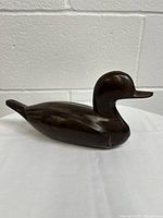 Side profile view of the dark wooden duck statue showing smooth polished finish and detailed carving of the head and body.