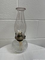 Front view of vintage oil lamp showing clear glass base, metal burner, and tall etched glass chimney.