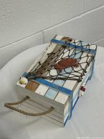 Angled top view of the white and blue striped wooden box with net and turtle decoration on a white table against a brick wall.