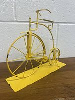 Full side view of the yellow vintage bicycle metal sculpture showing front large wheel and frame details.
