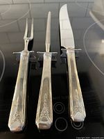 Carving fork, honing steel and knife front view on black surface