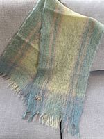 Full view of pastel plaid mohair scarf with fringes displayed on sofa