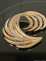 Front view of gold-tone feather swirl brooch