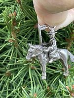 Front view of silver Mountie on horse charm with foliage background