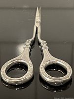 Full view of sterling scissors laid flat showing engraved handles and pointed blades
