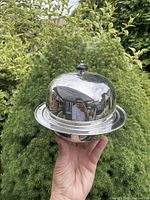 Complete three-piece silver muffineer held aloft showing dome lid with ebony finial seated on tray and base