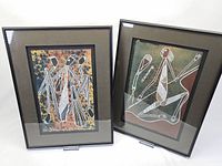 Two framed Indigenous art prints placed side by side, showing the black metal frames, quality matting, and the traditional Indigenous art styles with white line drawings on colored backgrounds.