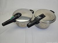 Two stainless steel pressure cookers side by side on white background, showing handles and lids