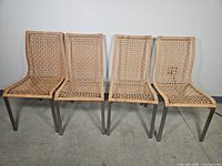 Four rattan bamboo chairs with woven seats and backs and metal legs, front view showing overall condition.