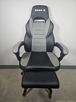 Front view of black and gray Bossin gaming chair with adjustable footrest extended, showing wear on armrests.
