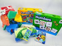 Lot overview showing the set of plastic beach toys, rolled turtle towel, and three boxed puzzles with themes including numbers, shapes, and Mickey Mouse.