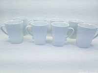 Eight white Corelle Coordinates coffee cups arranged showing embossed swirl patterns and handle placement.