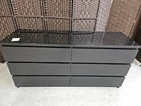 Front view of black Ikea Malm dresser showing six drawers and glass or glossy top surface