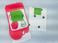 Set of Kate Spade kitchen accessories including red and green fruit print oven mitt and potholder, white dish towel with black polka dots, and apron folded underneath