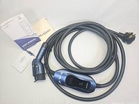 Image showing the Mustart branded electric car charging cable coiled, including the control unit with display and Type 2 connector, alongside printed user manual and instruction booklet.